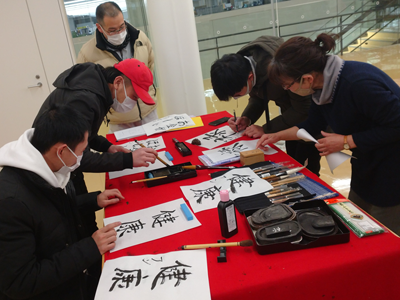 Foreign citizens trying calligraphy, assisted by exchange supporters
